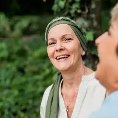 Zwei Frauen lachen im Freien. Die vordere Frau trägt ein Kopftuch und wirkt durch psychoonkologische Beratung gestärkt.