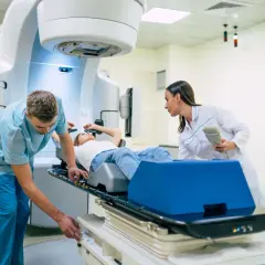 Ein Patient liegt auf einer Liege, während ein Techniker und eine Ärztin eine perkutane Strahlentherapie vorbereiten.