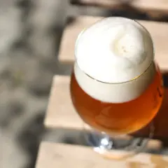 Ein Glas Bier mit viel Schaum steht auf Holzplanken. Vorsicht bei der Einnahme von Letrozol und Alkohol.