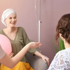 Freundinnen geben einer Frau mit Krebs während der Chemotherapie aufmunternde Worte und halten Ballons.