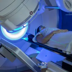 Frau liegt auf Liege unter Bestrahlungsgerät. Grüne Laserlinien markieren die Position. Strahlentherapie Brustkrebs Erfahrungen.