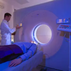 Arzt bedient CT-Scanner, Patient liegt auf Liege. Die CT-Strahlenbelastung wird minimiert.