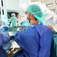 Chirurgen im OP-Saal bereiten sich auf eine onkologische Chirurgie vor, mit Fokus auf einem Monitor, der das Operationsfeld zeigt.