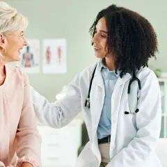 Ärztin mit Stethoskop legt Hand tröstend auf Schulter einer Patientin. Ein Gespräch über gynäkoonkologische Themen findet in einer freundlichen Atmosphäre statt.