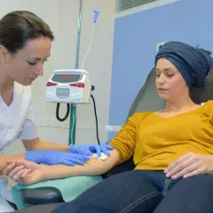 Eine Krankenschwester bereitet eine Infusion vor. Die Patientin, die eine Kopfbedeckung trägt, erhält die Behandlung, ein Zeichen dafür, dass die Chemo wirkt.