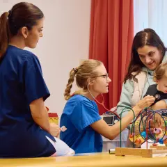 Ärzte in Krebszentren Deutschland untersuchen ein Kleinkind. Eine Krankenschwester hört mit dem Stethoskop ab, während eine Kollegin zusieht.