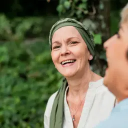 Zwei Frauen lachen im Freien. Die vordere Frau trägt ein Kopftuch und wirkt durch psychoonkologische Beratung gestärkt.