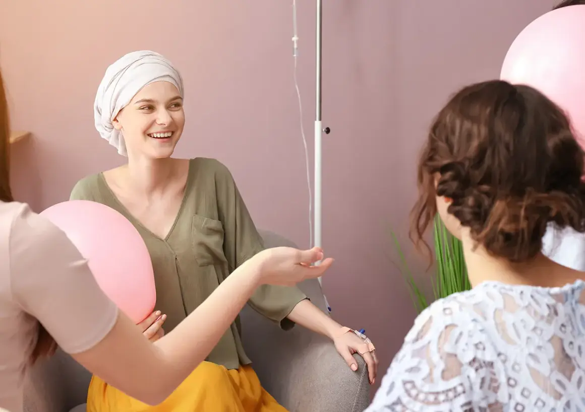 Freundinnen geben einer Frau mit Krebs während der Chemotherapie aufmunternde Worte und halten Ballons.