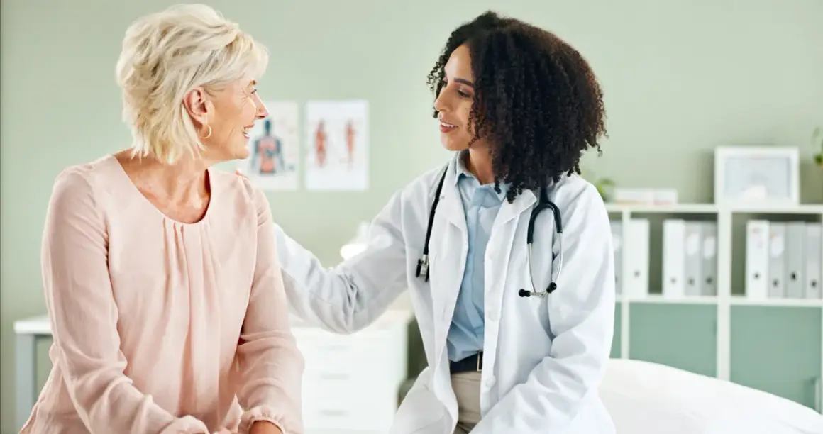 Ärztin mit Stethoskop legt Hand tröstend auf Schulter einer Patientin. Ein Gespräch über gynäkoonkologische Themen findet in einer freundlichen Atmosphäre statt.