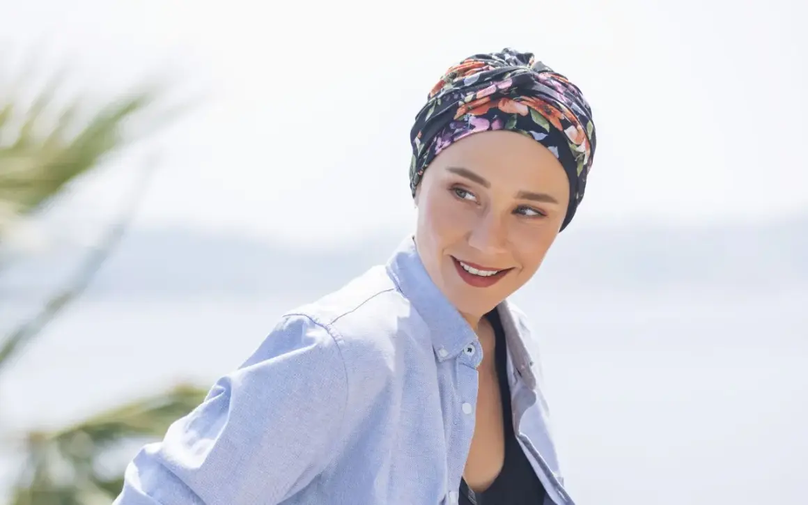 Frauen mit einem gebundenen Kopftuch, das sie während der Chemo tragen, lächeln zuversichtlich in die Kamera.