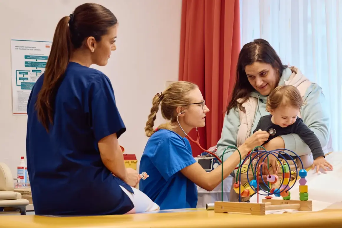 Ärzte in Krebszentren Deutschland untersuchen ein Kleinkind. Eine Krankenschwester hört mit dem Stethoskop ab, während eine Kollegin zusieht.