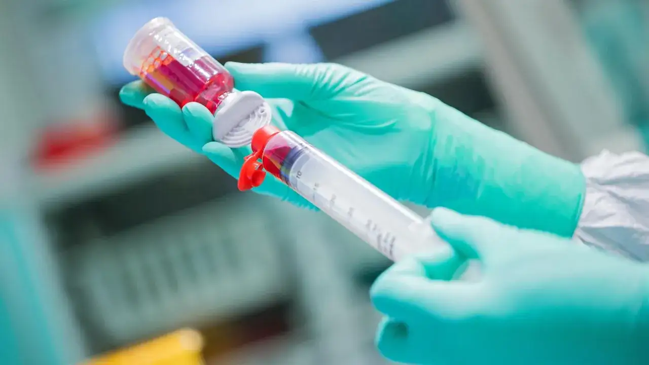 Hände in grünen Handschuhen ziehen rote Flüssigkeit aus einer Ampulle in eine Spritze. Dies ist eine wichtige Vorbereitung für eine Chemotherapie.