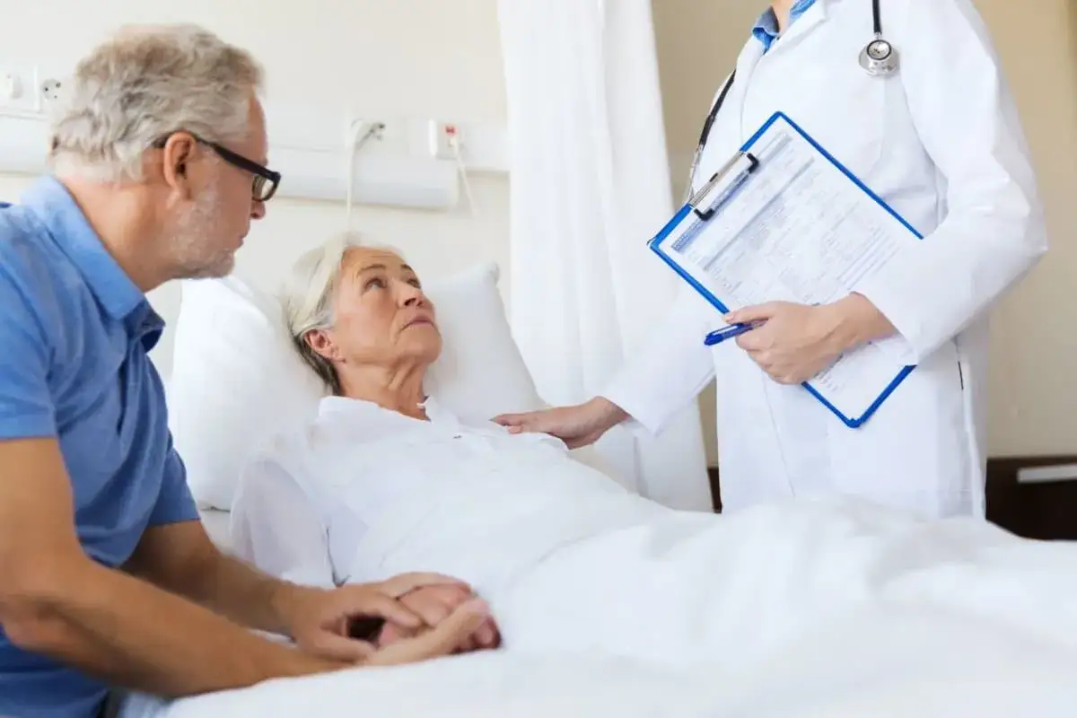 Älteres Paar im Krankenhaus. Frau liegt im Bett, Mann hält ihre Hand. Arzt mit Akte spricht über die Chemotherapie abgelehnt prognose.