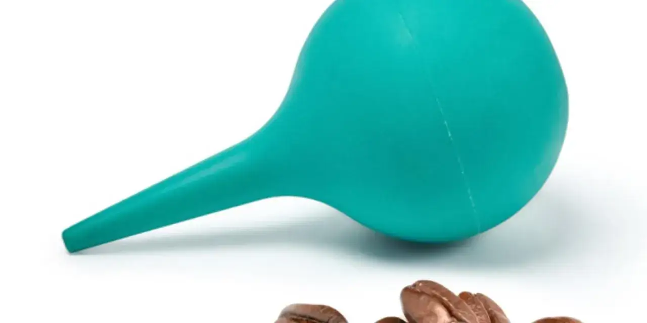 Türkisblaue Klistierspritze und Kaffeebohnen. Mögliche Verbindung zu Gerson Therapie Erfahrungen, die oft alternative Heilmethoden einschließt.