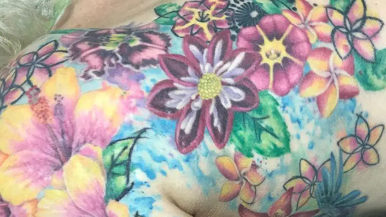 Ein farbenfrohes Blumen-Tattoo, das Lebensfreude nach einer Krebserkrankung symbolisiert. Hibiskus und andere tropische Blüten bedecken die Haut.