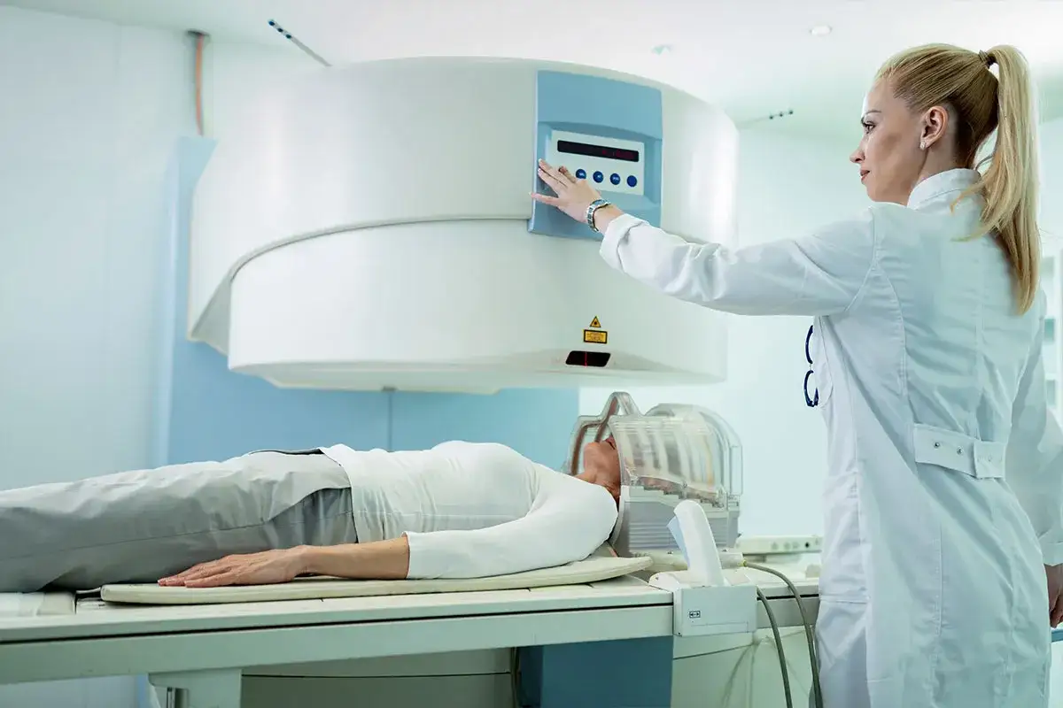 Ärztin bedient Gerät für Bestrahlung bei Brustkrebs. Patientin liegt auf Liege.