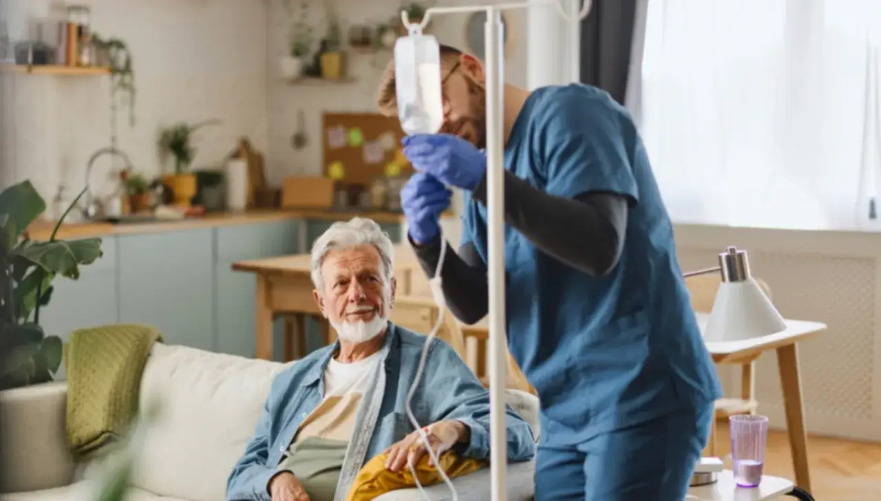 Ein älterer Mann erhält zu Hause eine Immuntherapie-Infusion. Ein Pfleger bereitet die Infusion vor.